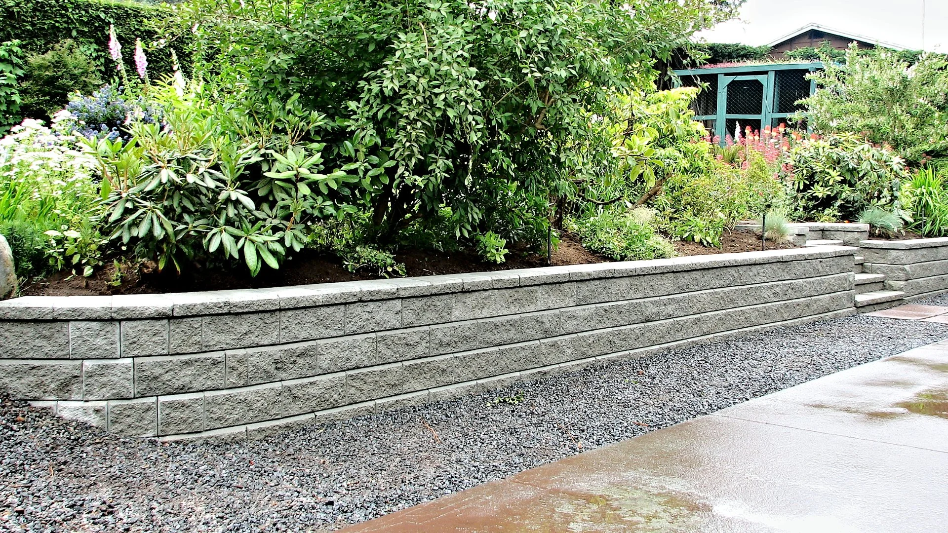 Garden landscape featuring a gray stone retaining wall with lush greenery and flowering plants