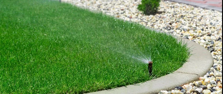 Sprinkler irrigation system spraying water onto a lawn near a rock landscape bed in Tulsa, OK.